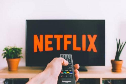 hand holding remote control pointed towards television showing Netflix logo