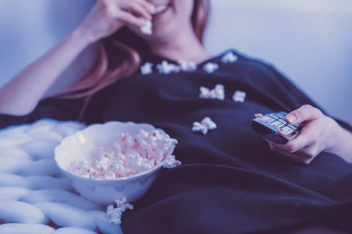 woman eating popcorn while holding remote