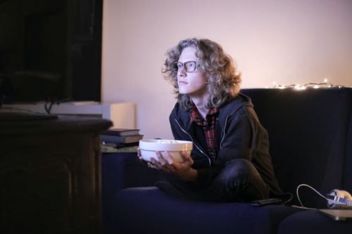curly haired man watching tv intently while holding bowl