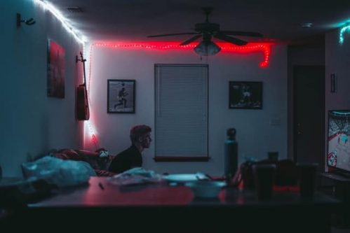 man watching TV in room with neon lights